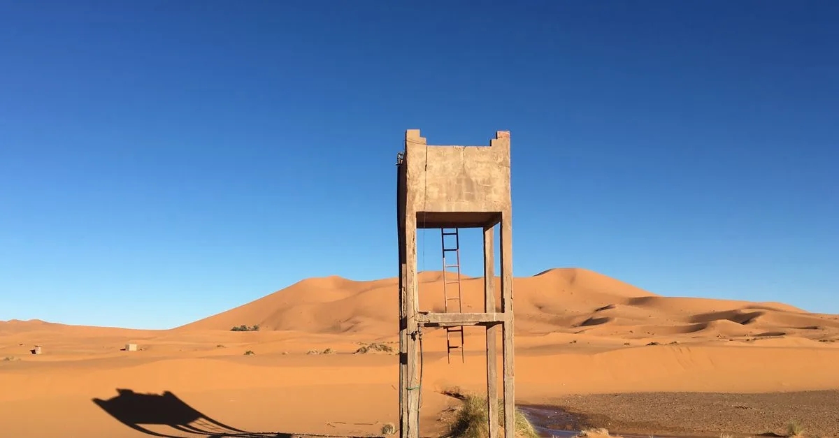 Concrete structure standing amidst the vast Merzouga sand dunes under a clear blue sky.