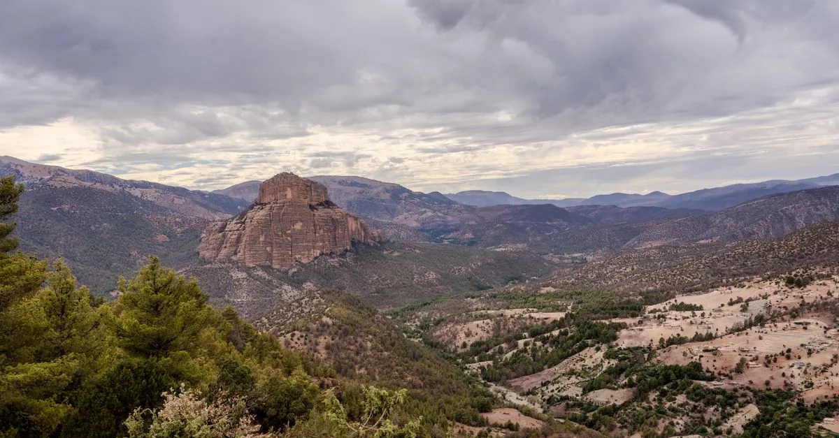 Vast landscape of Atlas Mountains in Tilouguite, Morocco with lush greenery and cloudy sky.