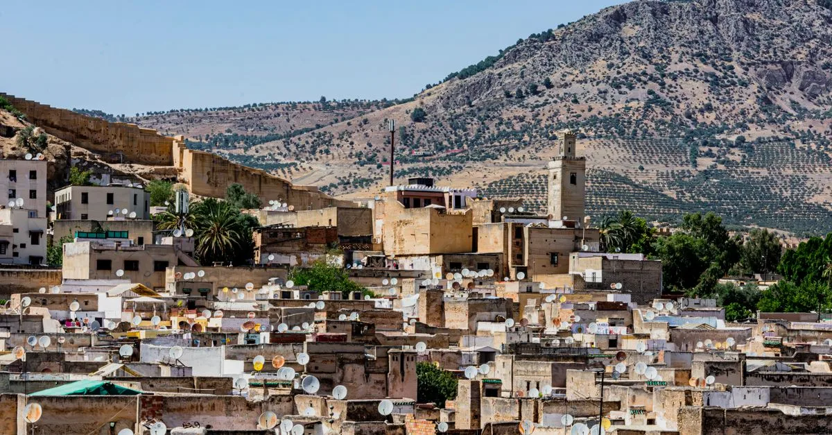 Explore the vibrant rooftops of Fes with satellite dishes, against a backdrop of Moroccan mountains.